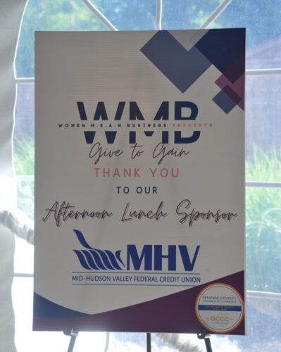 Event sponsor sign reading 'Give to Gain' with MHV logo and Mid-Hudson Valley FCU branding visible at bottom left of poster.