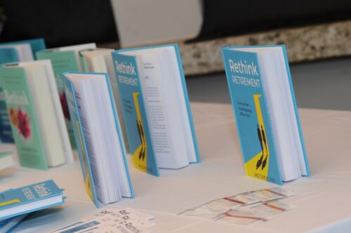 Row of blue books titled 'Rethink Retirement' standing upright on a white table.