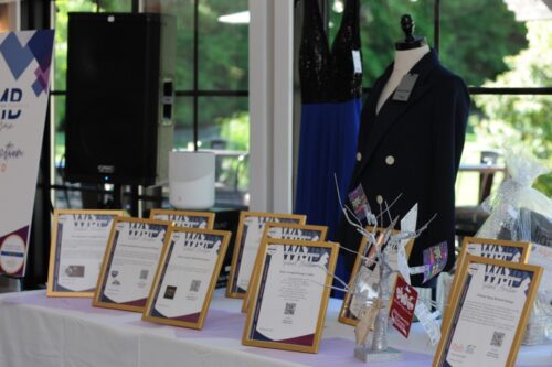 Display table of framed award certificates with a decorative centerpiece; mannequins and a banner in a bright showroom.