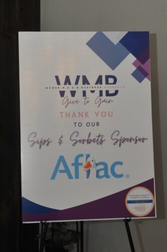 Sponsor board for an event featuring 'Give to Gain' messaging, with the Aflac logo (duck) and the Orange County Chamber of Commerce seal in the corner.